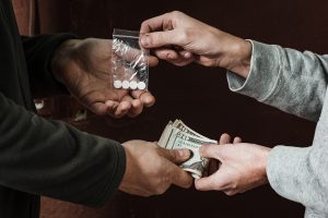 A close-up of two people in sweatshirts exchanging drugs for money.
