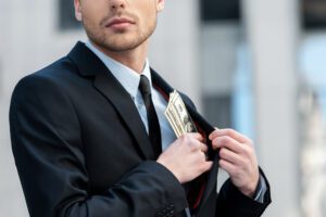 A person tucks a stack of money into the inside of their black suit jacket
