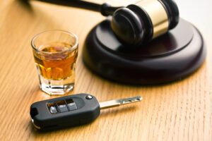 A gavel is placed on its side next to a shot glass full of alcohol and a car key.