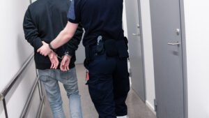 A person is handcuffed and escorted down a hallway by a police officer.