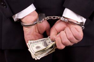 A person in handcuffs is holding a wad of $100 bills.