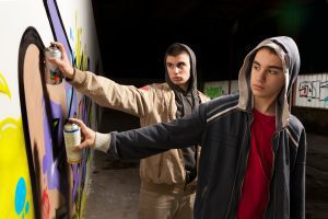 Two teens using spray paint to graffiti a wall