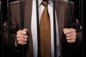 man in a brown suit and white collar shirt behind jail bars