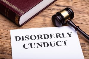A paper that reads “Disorderly Conduct” next to a gavel and a large law book.