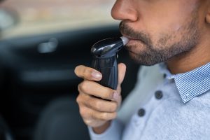 A man takes a breathalyzer test while sitting in a car.