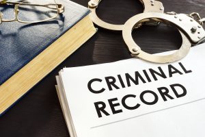 A law book with glasses on top next to a pair of handcuffs and a stack of papers that reads "Criminal Record."